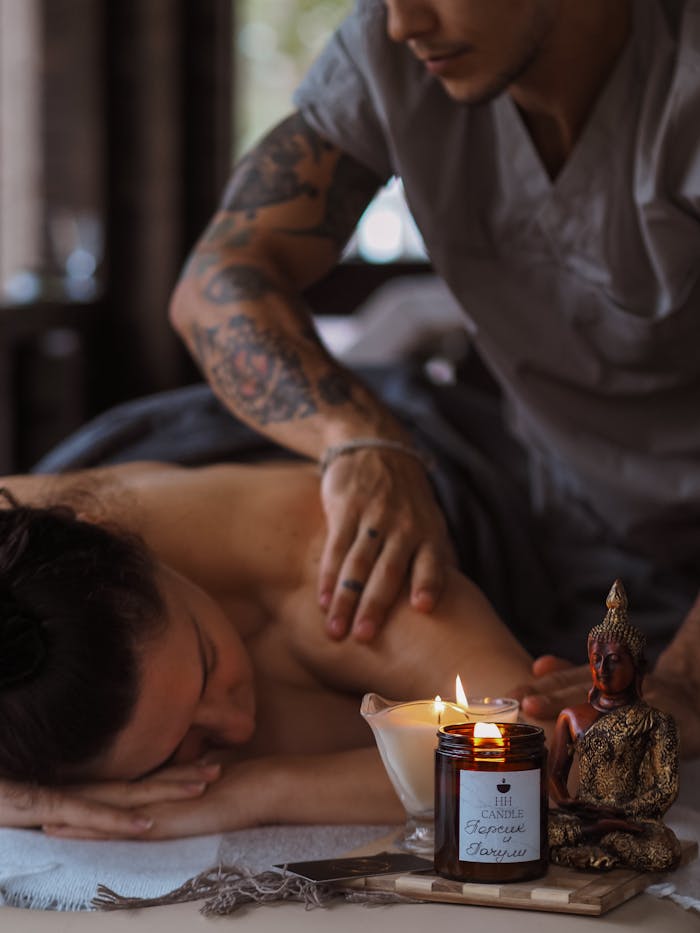 Tattooed massage therapist providing a relaxing spa treatment with candles for ambiance.